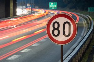 Placa de limite de velocidade de 80 km/h em rodovia movimentada durante a noite, com rastros de luz dos veículos