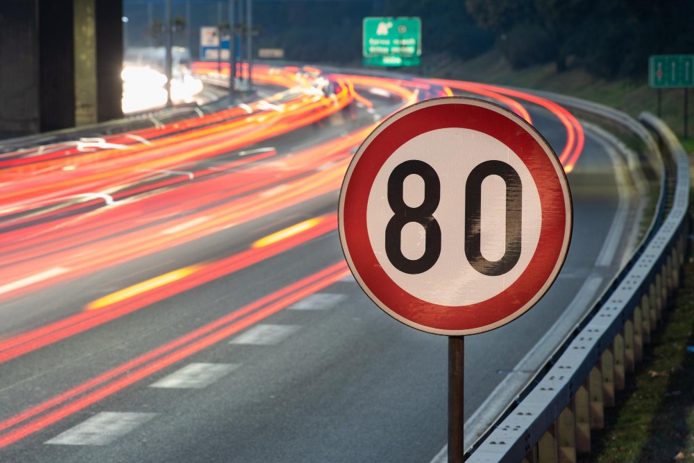 Placa de limite de velocidade de 80 km/h em rodovia movimentada durante a noite, com rastros de luz dos veículos