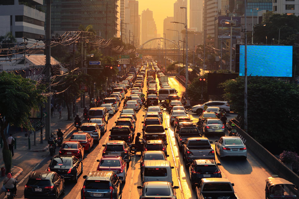 Trânsito intenso em avenida de grande cidade ao entardecer, com congestionamento de veículos e motocicletas.