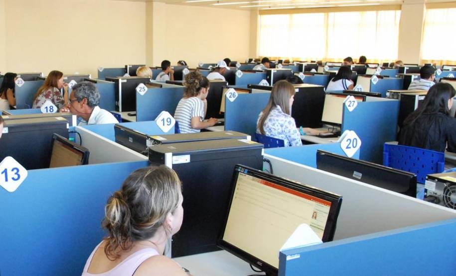 Candidatos realizando o exame teórico do DETRAN em um centro de testes com computadores individuais, ambiente organizado e numerado, etapa obrigatória para obtenção da CNH.
